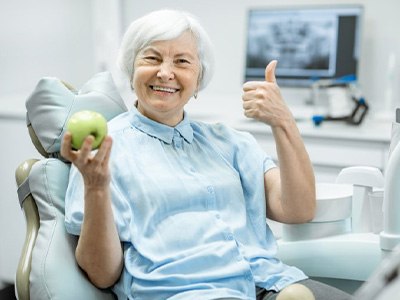 Woman with dental implants holding up an apple and a thumbs up